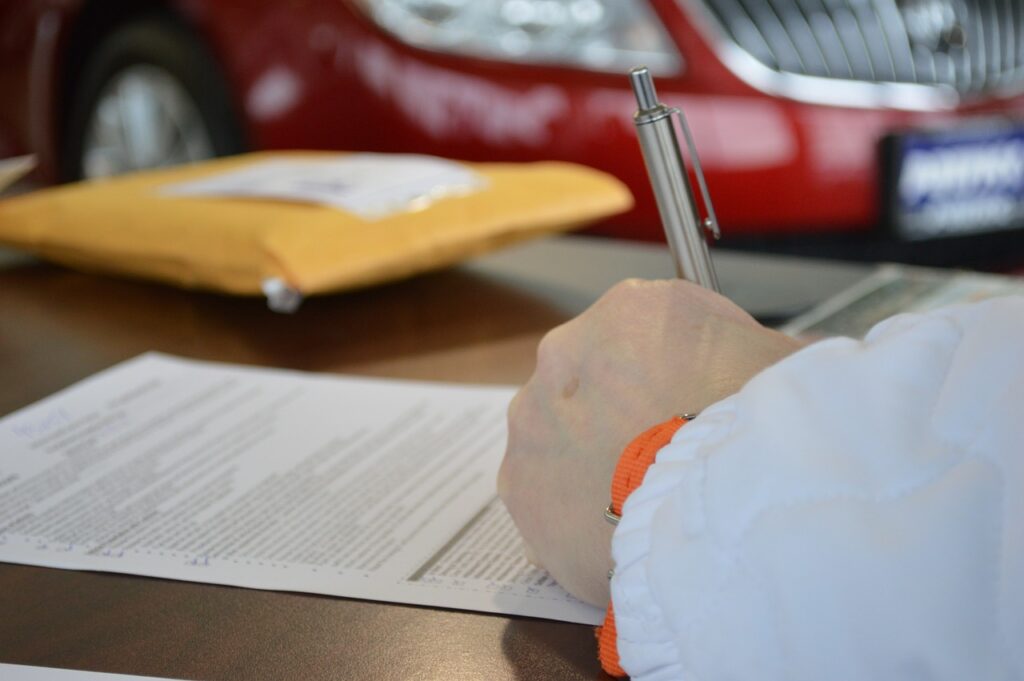 Man signs loan documents at car dealership while perhaps discussing personal loan interest rates.